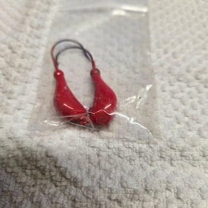May include: Two red fishing lures with a hook on each end. The lures are in a clear plastic bag.