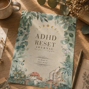 Puede incluir: Un diario rectangular con cubierta beige que presenta ilustraciones botánicas verdes de hojas, setas y polillas. El texto dice ADHD RESET JOURNAL y be kind to your mind. Un arco de fase lunar dorado está impreso sobre el título.