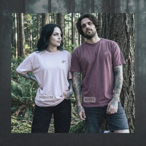 May include: Two short-sleeved crew neck t-shirts. One is a light pink shirt labeled Blossom with the word angel printed on the chest. The other is a dark berry red shirt labeled Berry with the word angel printed on the chest. Both shirts are plain.