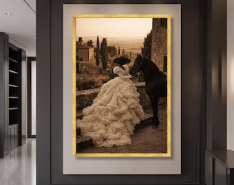 May include: A framed wall art print featuring a person in a voluminous, tiered cream-colored gown and a wide-brimmed black hat standing next to a black horse on a stone terrace, with a landscape of trees and buildings in the background.