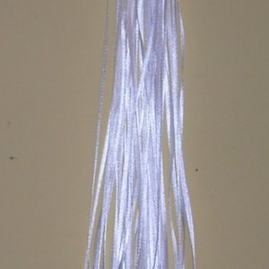 May include: A bundle of white satin ribbon with silver pacifier charms attached. The ribbon is tied together at the top and the charms are hanging down.