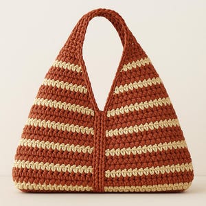 May include: A handmade crochet tote bag in a warm terracotta color with horizontal cream-colored stripes. The bag features a wide, open top and a single, sturdy handle. The bag's design is simple and stylish, perfect for carrying everyday essentials.