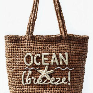 Puede incluir: Un bolso tote tejido marrón con asas trenzadas. El bolso presenta las palabras "OCEAN breeze!" en escritura blanca, junto con un diseño de estrella de mar y olas. Este bolso de playa es ideal para llevar lo esencial.