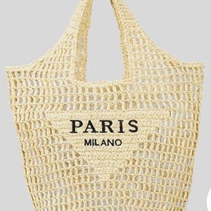 May include: A beige woven tote bag with a large open weave design. The bag has a rectangular shape with a wide opening and a single handle. The words "PARIS MILANO" are printed in black on the front of the bag.
