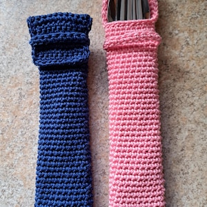 May include: Two handmade crochet utensil holders. One is navy blue, the other is light pink. The navy blue holder is empty, while the pink holder contains silverware. Both are rectangular with a folded top.