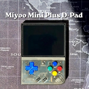 Może przedstawiać: Przezroczysta konsola do gier przenośna Miyoo Mini Plus D-Pad. Urządzenie posiada czarny ekran, niebieski D-pad i kolorowe przyciski akcji. Widoczny jest tekst "Miyoo Mini Plus D-Pad".