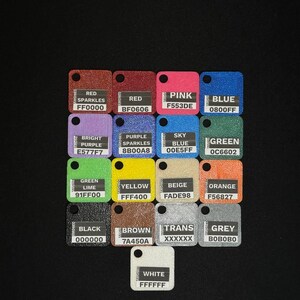 May include: A collection of small, square color swatches with rounded corners and a hole at the top. Each swatch displays a different color name and its corresponding hexadecimal code, including red, pink, blue, and green.