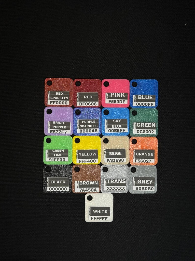 May include: A collection of small, square color swatches with rounded corners and a hole at the top. Each swatch displays a different color name and its corresponding hexadecimal code, including red, pink, blue, and green.
