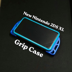 Puede incluir: Una consola New Nintendo 2DS XL negra con una funda protectora azul. La consola tiene una superficie texturizada y un borde azul. Las palabras "New Nintendo 2DS XL" y "Grip Case" están impresas en blanco.