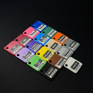 May include: A collection of small, color-coded rectangular tags with rounded corners, each displaying a different color name and hexadecimal code. Colors include red, pink, blue, green, yellow, and black. The tags are arranged on a black surface.