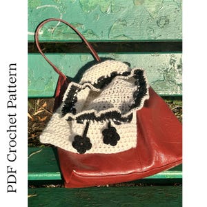 May include: A red leather tote bag with a cream crocheted bag inside. The crocheted bag has black trim and two black flower appliqués. The text "PDF Crochet Pattern" is on the left side of the image.