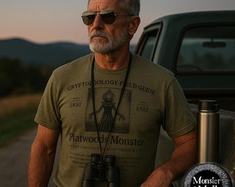 May include: A green t-shirt with a black and white illustration of a creature with a hood and the text "Cryptopzoology Field Guide 1932 1982 Platwoods Monster Brayton County West Virginia ETA".