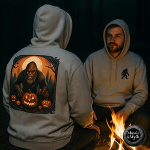 May include: Two grey hooded sweatshirts. One has a large graphic of a Bigfoot with a carved pumpkin and a full moon. The other has a small Bigfoot silhouette. The sweatshirts are from the Monster & Myth collection.