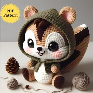 May include: A crocheted squirrel amigurumi wearing a green hooded jacket. The squirrel has brown and white fur, large black eyes, and a pink nose. The squirrel is sitting on a white surface with a brown pine cone and a ball of yarn.