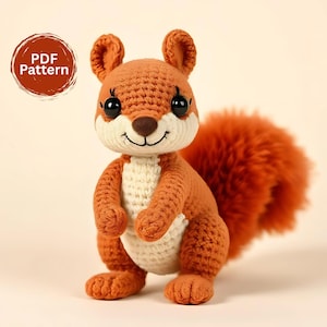 Op de afbeelding: Een handgemaakte gehaakte eekhoorn in tinten oranje, crème en bruin. De eekhoorn heeft een pluizige staart, grote zwarte ogen en een lachend gezicht. De afbeelding bevat een cirkelvormige afbeelding met de tekst "PDF Pattern".