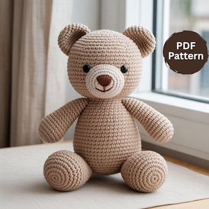 Może przedstawiać: Szydełkowy miś w odcieniach beżu i kremu, z czarnymi oczami i brązowym nosem. Miś ma okrągłą głowę, małe uszy i siedzi z wyciągniętymi ramionami i nogami. Obraz zawiera okrągłą grafikę z tekstem "PDF Pattern".