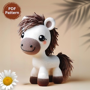 Op de afbeelding: Een gehaakt wit en bruin paard met een vriendelijke uitdrukking. Het paard heeft een bruine manen en staart, met een wit lichaam en bruine hoeven. De tekst "PDF Pattern" staat in een bruine cirkel linksboven. Een madeliefje staat linksonder.
