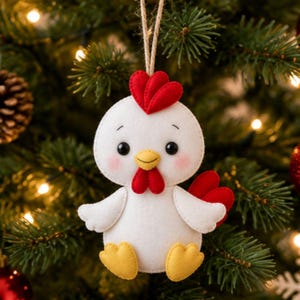 May include: A white felt chicken ornament featuring a red heart-shaped comb, a yellow beak, red wattles, and yellow feet. The chicken has black bead eyes and pink blush on its cheeks. A jute twine loop is attached to the top for hanging.