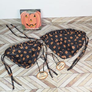 Può includere: Due fodere per cesti nere a tema Halloween con disegni di zucche arancioni e bordi a balze. Ogni fodera ha lunghi lacci neri. Due etichette ovali di legno recitano "Happy Halloween". È presente anche un libro Longaberger Jack O'Lantern Ties.