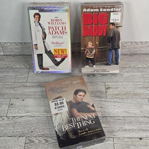 May include: Three VHS tapes are displayed. The titles are "Patch Adams" starring Robin Williams, "Big Daddy" starring Adam Sandler, and "The Next Best Thing". The tapes are in their original packaging.