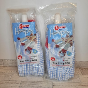 May include: Two Quickie HomePro Ring-A-Mop Refills in clear plastic packaging. The mop heads are white with a blue grid pattern. The packaging has a blue background with the Quickie HomePro logo and product information.