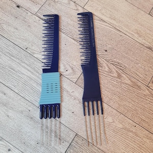 May include: Two dark blue hair picks with metal tines. One pick has a light blue grip with a series of small rectangular holes. The other pick has a simple design. Both are on a light wood grain surface.