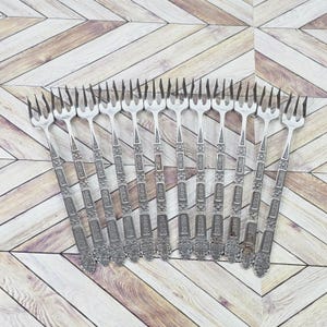 May include: A collection of twelve silver forks with decorative handles. The forks are fanned out, highlighting their design. The handles have a repeating pattern of rectangular and floral details, adding to their elegance.