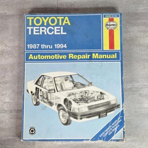 May include: A blue Haynes automotive repair manual for a Toyota Tercel, covering model years 1987 through 1994. The cover features a white line drawing of a car with an exposed engine and interior, along with the text 92085 (2106) and OWM 2106.