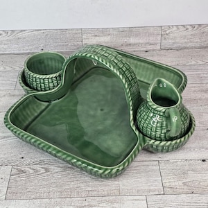 Könnte beinhalten: Ein grünes Keramik-Servierset mit Korbgeflecht-Design. Das Set enthält ein herzförmiges Tablett, ein rechteckiges Tablett, einen kleinen Krug und eine Tasse. Das Set ist zum Servieren von Snacks oder Vorspeisen gedacht.