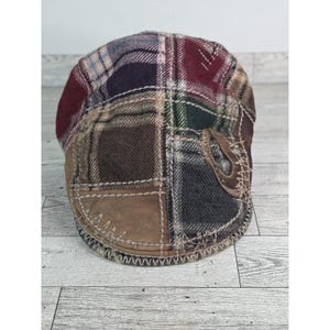 May include: A multi-coloured patchwork newsboy cap. The cap features a stitched brim and a textured, multi-panel design. The colours include brown, burgundy, green, and blue. The hat is made of a woven fabric.