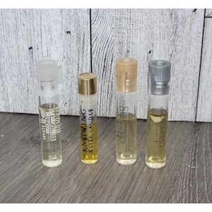 May include: Four perfume sample vials. The vials are clear glass with various coloured caps. The first vial has a clear cap and the text "White Linen Breeze Estee Lauder". The second vial has a gold cap and the text "Knowing Estee Lauder". The third and fourth vials have the text "dazzling".