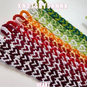 Könnte beinhalten: Eine Sammlung gewebter Freundschaftsarmbänder mit einem sich wiederholenden Herzmuster in einem Farbverlauf aus Dunkelrot, Hellrot, Orange, Gelb und Grün, wobei der Text KNOTSBYDANNA und HEART CUSTOM BRACELETS zu sehen ist.