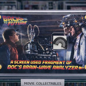 May include: A framed movie collectible featuring a scene from "Back to the Future." The image includes the film's logo and text: "A Screen Used Fragment of Doc's Brain-Wave Analyzer." The collectible is displayed in a clear case.