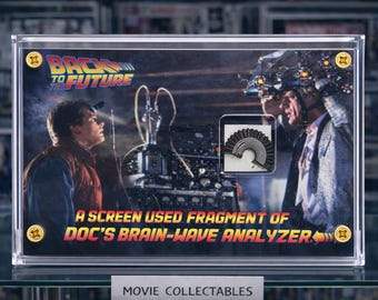 Puede incluir: Un objeto de colección de películas enmarcado, con una escena de "Regreso al Futuro". La imagen incluye el logotipo de la película y el texto: "A Screen Used Fragment of Doc's Brain-Wave Analyzer". El objeto se exhibe en una vitrina transparente.