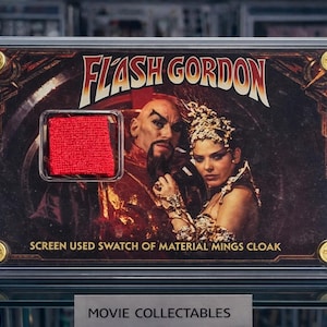 以下が含まれることがあります： 映画「フラッシュ・ゴードン」のタイトルとキャラクターが描かれた、額装された映画のコレクターズアイテム。 フレームには、ミンのマントの赤い布サンプルが含まれています。 コレクターズアイテムは、金色のコーナーアクセントが付いた透明な保護ケースに収められています。