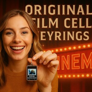 A smiling woman holding a small keychain with a picture on it, standing in front of a sign that says "ORIGINAL FILM CELL EYBRINGS" and a neon sign that says "INEMIA".
