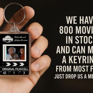 May include: A film cell keyring featuring a movie still, held in a hand. The keyring has a silver ring and the text "ORIGINAL FILM CELL". The background text says "WE HAVE 800 MOVIES IN STOCK AND CAN MAKE A KEYRING FROM MOST FILMS".