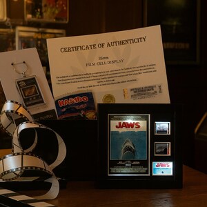 a framed poster of the movie "Jaws", a keychain, and a certificate of authenticity for a film cell display.