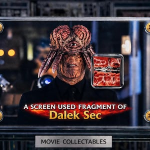 May include: A framed movie collectible featuring a Dalek Sec character. The character has a brown, brain-like head with a single eye and tentacles. The frame includes the text "A SCREEN USED FRAGMENT OF Dalek Sec" and "MOVIE COLLECTABLES".