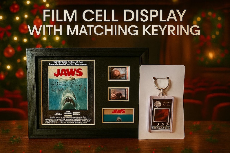 a framed poster of the movie "Jaws" with a keyring, a small keychain, and a framed picture of a shark. The background is blurred, but it appears to be a festive setting with Christmas lights.