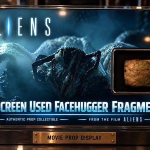 May include: A rectangular acrylic display case containing a small, textured, brownish-green fragment of a facehugger prop from the film Aliens. The display features the text ALIENS, A SCREEN USED FACEHUGGER FRAGMENT, and AUTHENTIC PROP COLLECTIBLE.