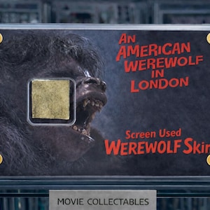 Op de afbeelding: Een ingelijst filmverzamelobject met een weerwolf uit "An American Werewolf in London". De display bevat een stukje gebruikte weerwolfhuid, met rode tekst en gouden accenten. Het item is gelabeld "Movie Collectables."