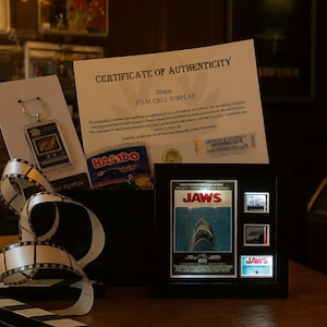 a framed poster of the movie "Jaws", a keychain, and a certificate of authenticity for a film cell display.