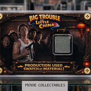 May include: A framed movie collectible from "Big Trouble in Little China." The image shows the film's title and cast, with a production-used material swatch. The frame has gold detailing. The collectible is displayed in a clear case.