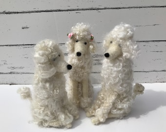 May include: Three white fluffy poodle dog figurines. The poodle in the center is wearing a pink flower crown.