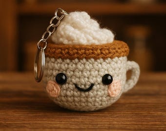May include: A crocheted coffee cup keychain with a smiling face, brown rim, and white whipped cream on top.