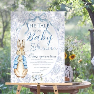 May include: A blue and white baby shower sign with a Peter Rabbit illustration. The sign says "The Tale of Our Baby Shower" and "Once upon a time..." with a floral design.