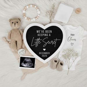 Könnte beinhalten: Baby-Ankündigung mit Teddybär, Buchstabenbrett mit der Aufschrift "We've been keeping a little secret December 2025", Baby-Body, Ultraschallbild, Babyschuhe und Holzperlenarmband.