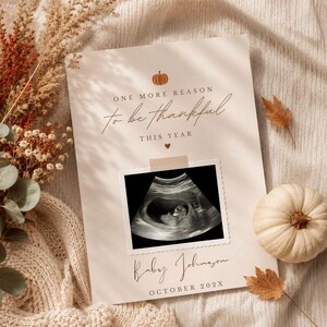 May include: A cream-colored announcement card featuring a small orange pumpkin icon, the text "ONE MORE REASON to be thankful THIS YEAR", a central ultrasound image, and the text "Baby Johnson OCTOBER 202X" printed in a dark brown serif font.
