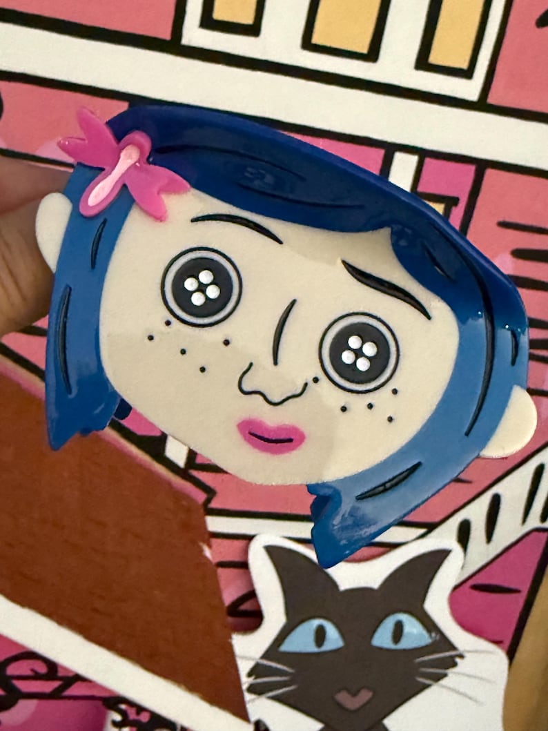 May include: A blue-haired cartoon character face with button eyes and a pink bow. The character has freckles and a pink mouth. The background features a pink and white house design and a black cat.
